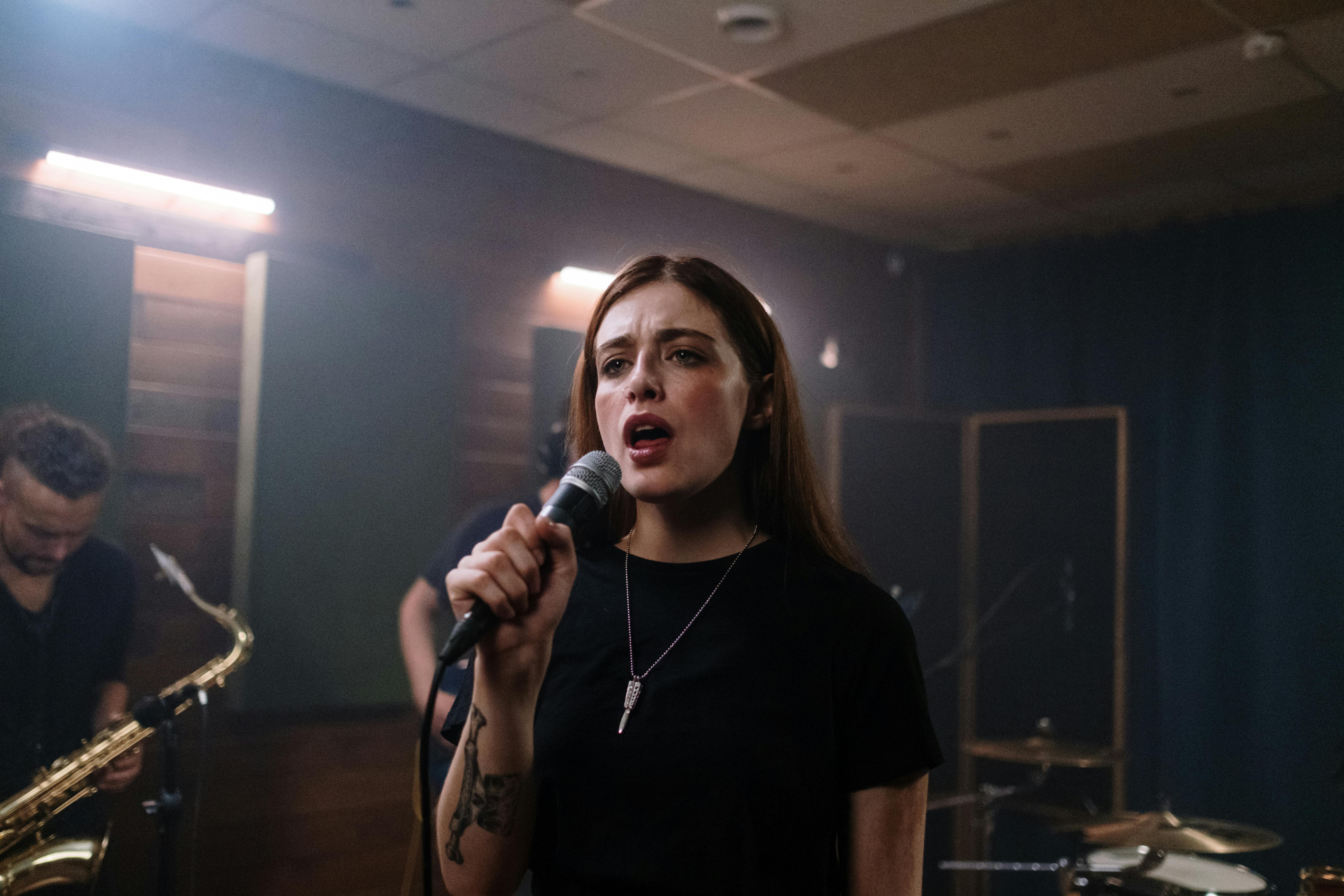 Young woman singing into a microphone during a band rehearsal.